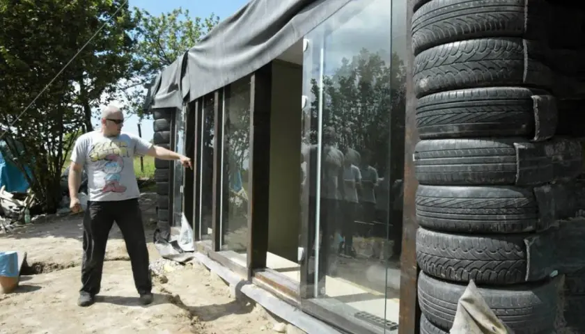 Budowa **earthship** z opon. Mężczyzna wskazuje na szklaną ścianę domu z opon.