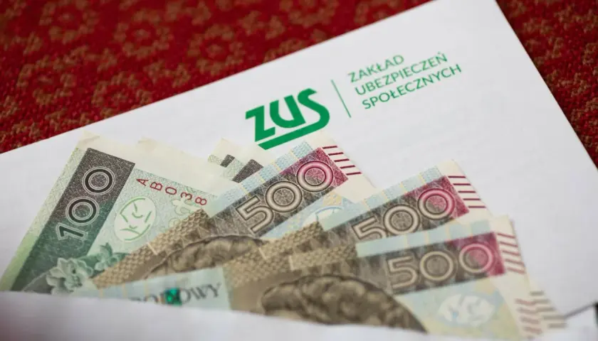 ZUS odszkodowania cennik tabela: banknoty 100 i 500 zł w kopercie z logo ZUS.