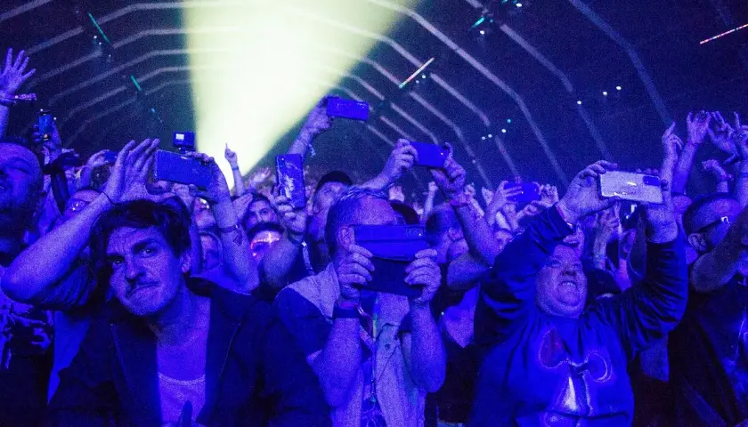 Tłum na fest festiwalu nagrywa koncert telefonami. Światła sceny oświetlają twarze ludzi.