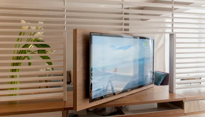 Ein moderner Wohnraum mit einem drehbaren Fernseher, der sich elegant in die Holzverkleidung integriert. Callas und dezente Beleuchtung schaffen eine ruhige Atmosphäre, ideal, um den Fernseher verstecken zu können.
