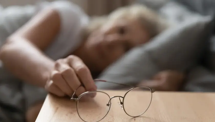 Kobieta sięga po okulary, czując wysokie tętno po przebudzeniu.
