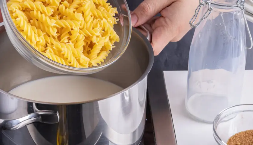 Eine Hand schüttet Spiralnudeln in einen Topf mit Milch. Zutaten für milch nudeln.