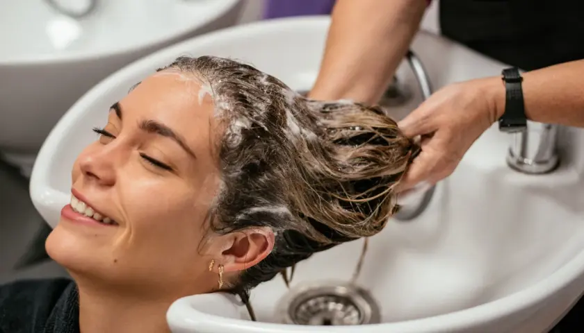 Una mujer sonríe mientras le lavan el pelo en un salón. La frecuencia con la que hay que lavarse el pelo varía, pero este momento de spa parece perfecto.
