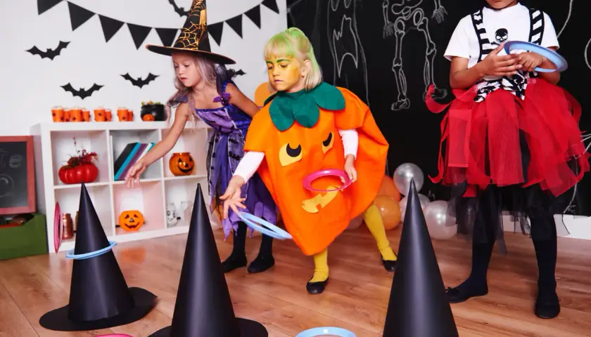 Niñas disfrutan de una divertida celebración de Halloween lanzando aros a sombreros de bruja.