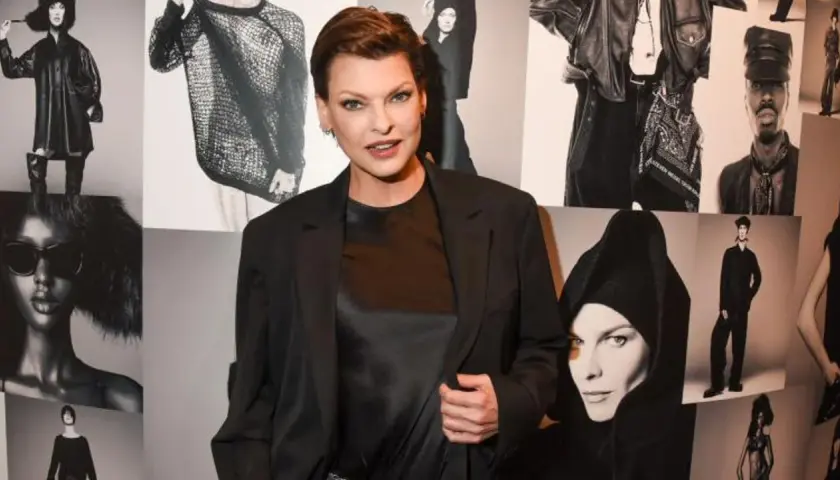 Linda Evangelista hoy, posando con confianza frente a un collage de sus icónicas fotos de moda.