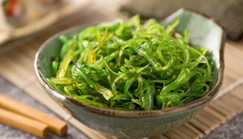 Insalata di alghe wakame in una ciotola, con bacchette. Informazioni su alga wakame controindicazioni.