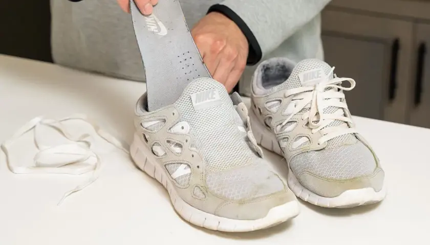 Man removes insole from dirty white Nike sneakers. Learn como quitar desteñido en zapatillas blancas.
