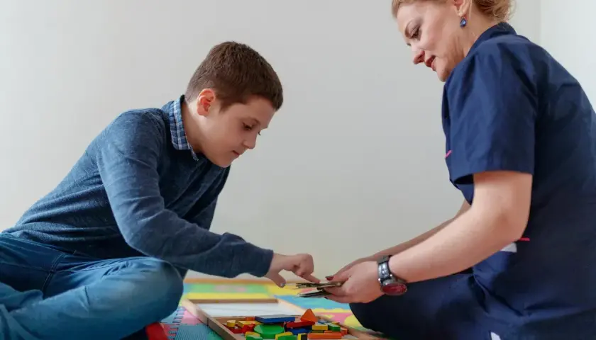 Chłopiec i terapeutka bawią się klockami w sali terapeutycznej.