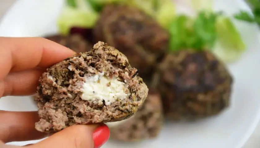 Kotlet mielony z serem w środku, trzymany w dłoni, na talerzu z sałatką.