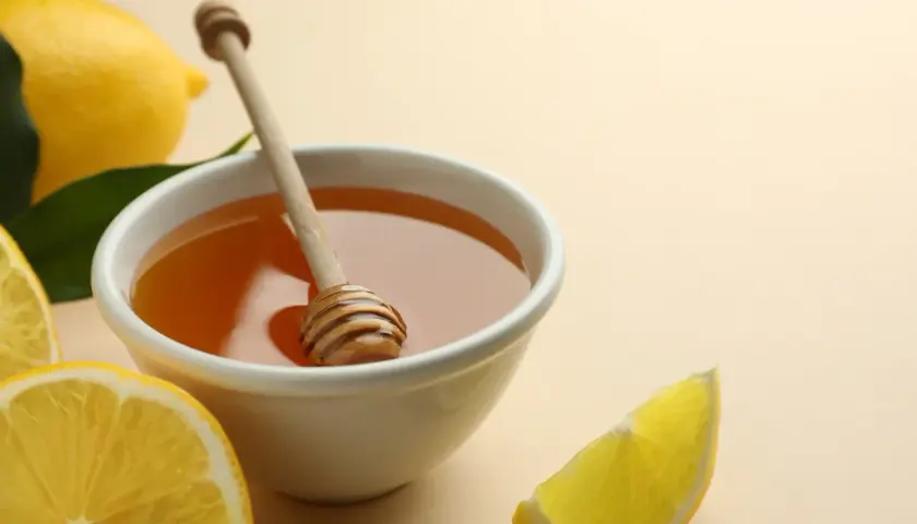 Un remède naturel contre le mal de gorge : un bol de miel doré avec une cuillère en bois, entouré de citrons frais et de feuilles vertes.