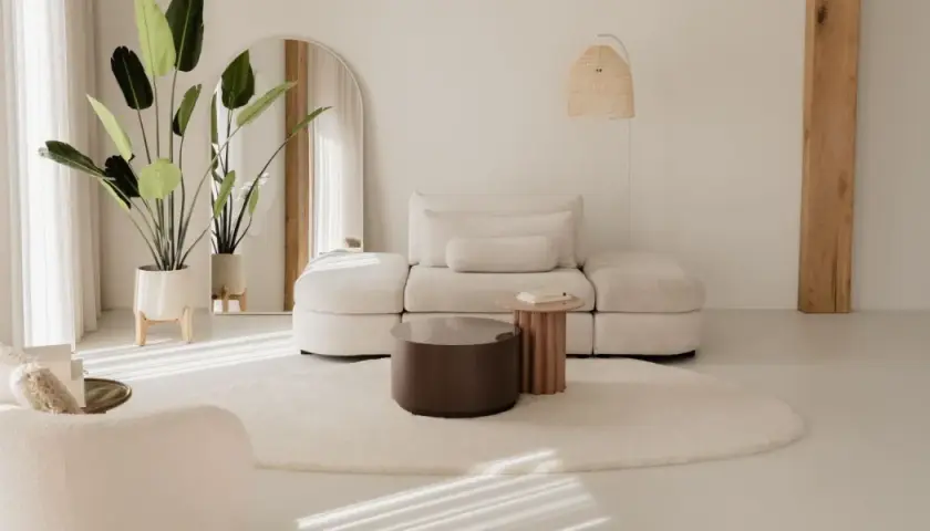 Ein helles Wohnzimmer im Japandi-Stil mit einem beigen Sofa, einem runden Teppich und einer großen Topfpflanze.