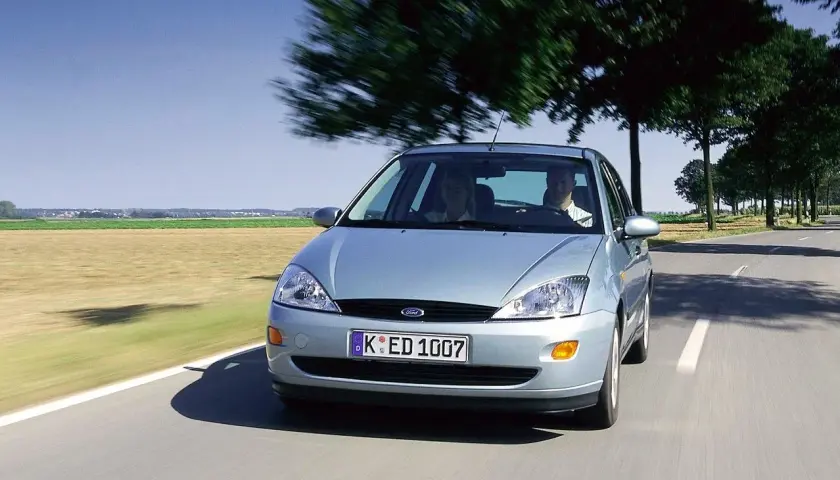 Srebrny Ford Focus MK1 1.6 benzyna w ruchu po wiejskiej drodze, z dwoma osobami w środku.