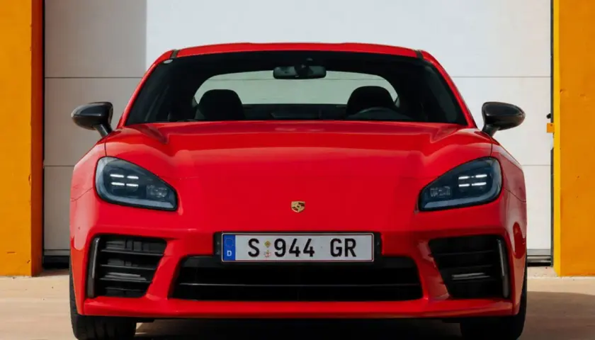 El llamativo Porsche 944 rojo, con su distintivo frontal y faros LED, se exhibe frente a una puerta de garaje blanca y paredes naranjas.