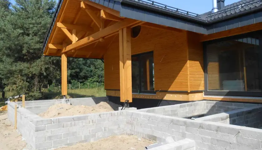 Drewniany dach krokwiowy nad wejściem do domu w budowie, z widocznymi belkami i elementami konstrukcyjnymi.