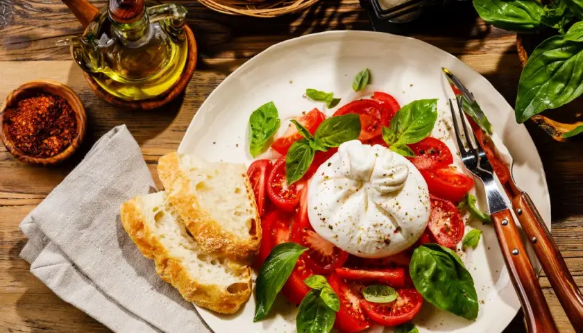 Pyszna burrata, czyli straciatella ser, z pomidorami i bazylią, podana z chrupiącym pieczywem i oliwą.