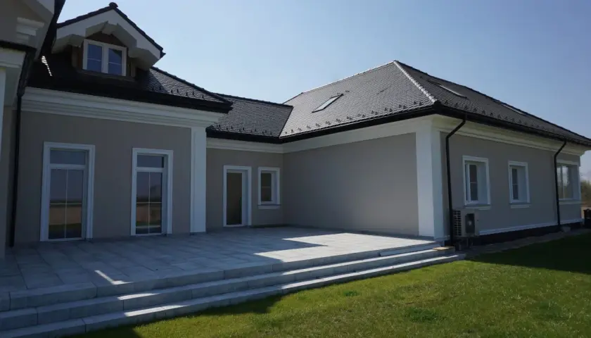 Elegancki dom z tarasem i trawnikiem. Biały gzyms podkreśla architekturę budynku.