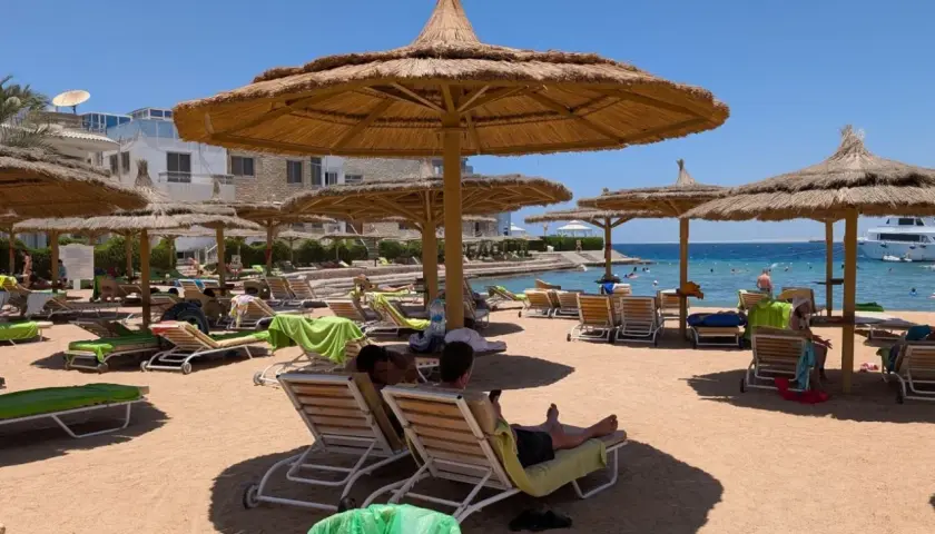 Egipt last minute all inclusive najtaniej: piaszczysta plaża z leżakami i parasolami, turkusowe morze, hotel w tle. Idealne miejsce na relaks.