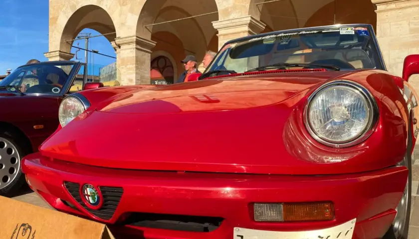 Dreaming of renting a car in Italy? This classic red Alfa Romeo convertible, parked under arched buildings, evokes the perfect Italian road trip.
