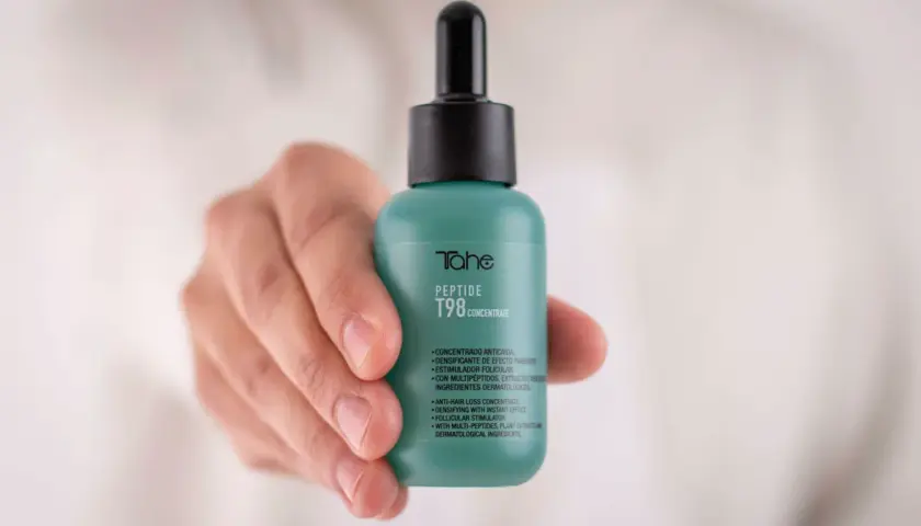 Mano sostiene frasco verde con peptidos para el pelo, concentrado anticaída T98 de Tahe.