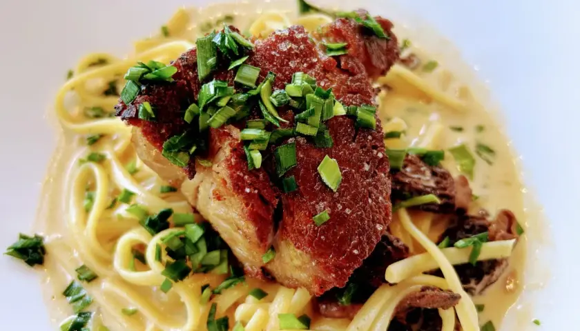 Un morceau d'échine de porc croustillante sur des pâtes crémeuses, garni de ciboule fraîche. Un délice !