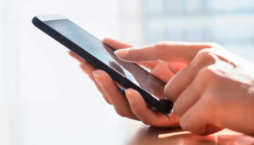 Dłoń dotyka ekranu smartfona, szukając archiwum SMS.