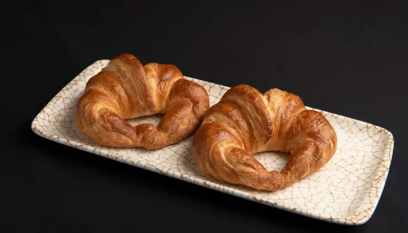 Dos croissants dorados, listos para disfrutar. El hojaldre crujiente invita a hacer croissant con hojaldre casero.