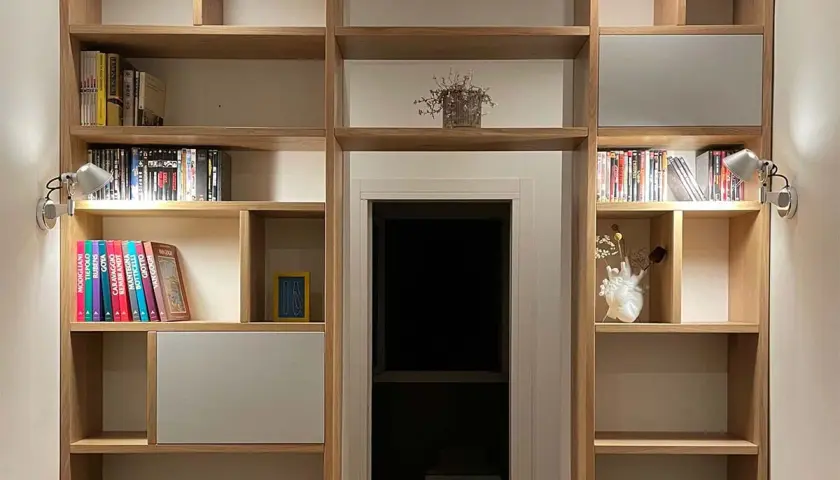 Parete in legno fai da te con libri, DVD e decorazioni. Illuminazione discreta valorizza gli oggetti.