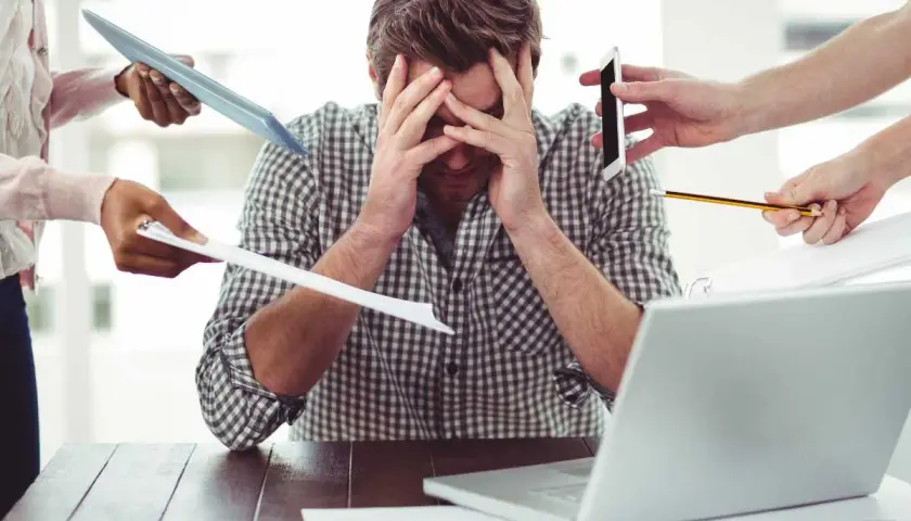 Uomo stressato, sommerso da richieste: tablet, fogli, telefono, matita. Il superlativo di busy è qui.