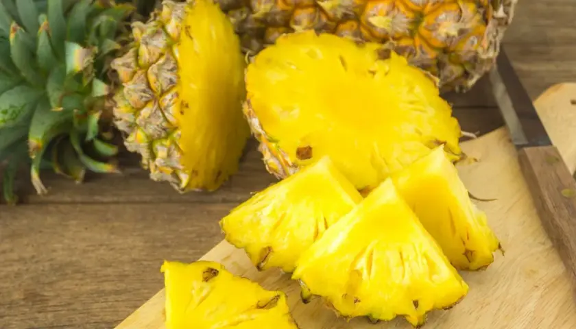 Soczyste kawałki ananasa na desce, obok całego owocu. Czy ananas jest zdrowy? Tak, to bomba witaminowa!