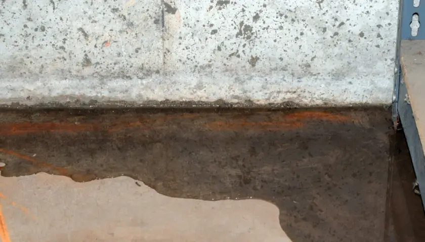 Wasser steht auf der Bodenplatte, ein Zeichen für einen hohen Grundwasserspiegel. Rostige Spuren deuten auf Feuchtigkeit hin.