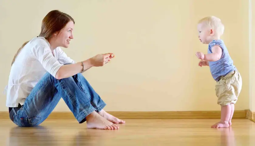 Mamma incoraggia il suo bambino, che sta imparando quando iniziano a camminare i bambini, a fare i suoi primi passi.