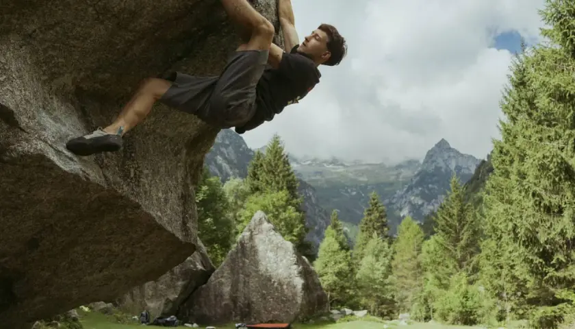 Mężczyzna wspina się po skale w górach, stosując zasady boulderingu. W tle piękne krajobrazy.