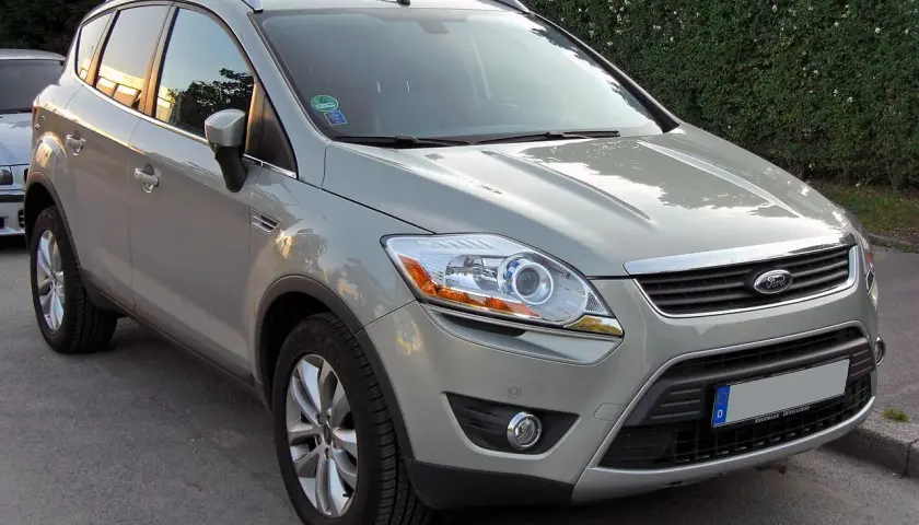 Szary Ford Kuga, SUV, prezentuje swoje wymiary na tle zielonego żywopłotu.