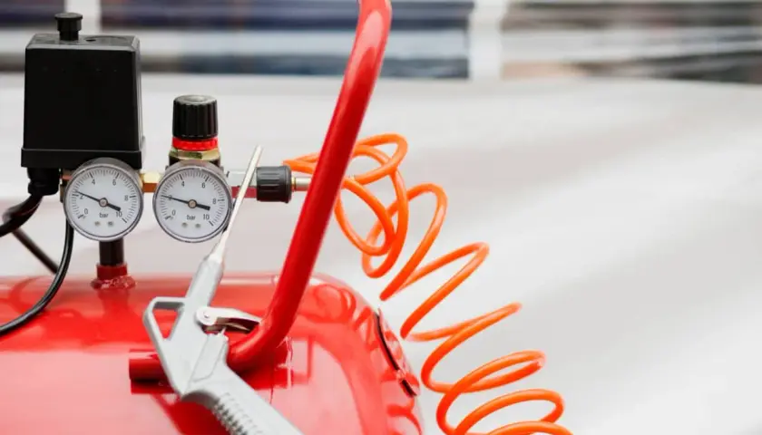 Detalles de un compresor de aire rojo con manómetros y pistola. Aprende como limpiar un compresor de aire para un óptimo funcionamiento.