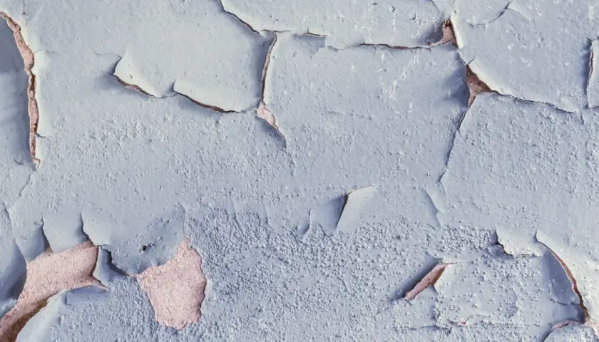 Texture d'une peinture qui s'écaille, révélant la texture rugueuse du mur sous-jacent, témoignant de l'humidité.