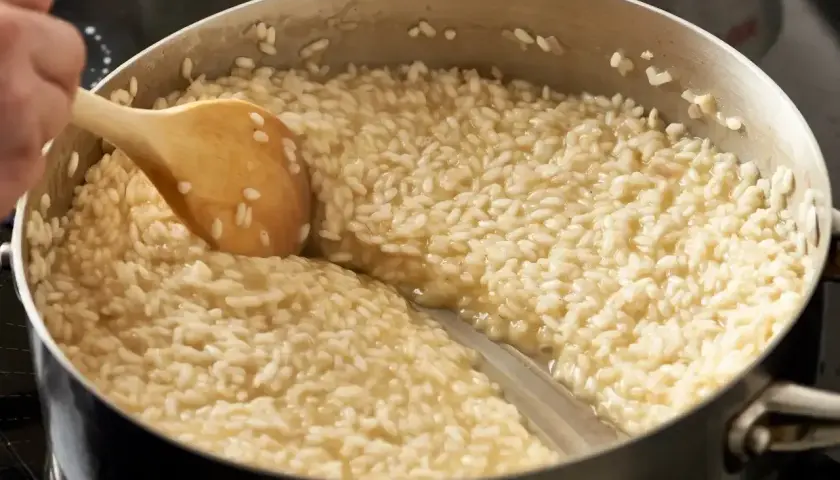 Drewniana łyżka miesza kremowy ryż do risotto w garnku.
