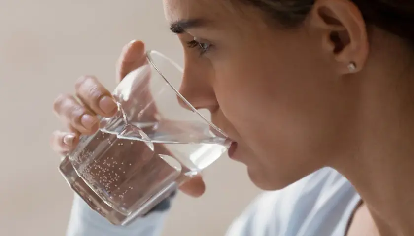 Kobieta pije wodę z kieliszka, wykonując test na odwodnienie.