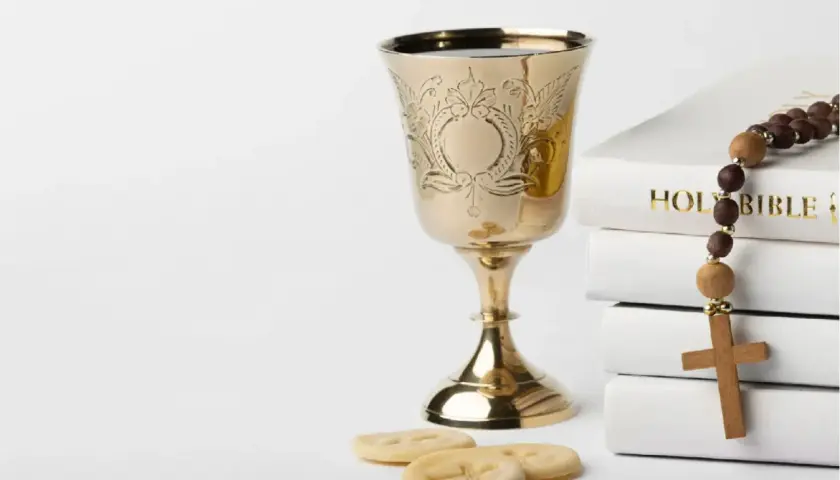 Złoty kielich, stos białych ksiąg z napisem "HOLY BIBLE", różaniec i opłatki. Symbolika sakramentu, który może być odnotowany w akcie chrztu.