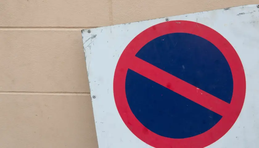 Znak zakaz postoju na tle beżowej ściany.