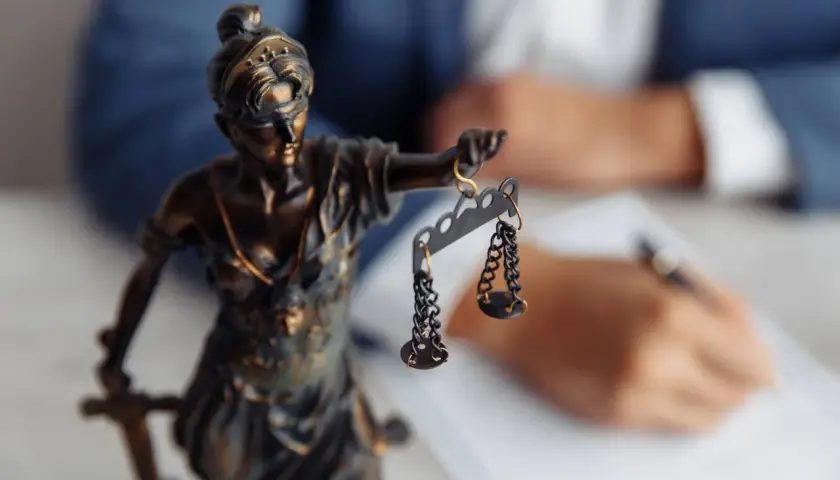 Figurka Temidy z wagą symbolizuje sprawiedliwość. W tle prawnik sporządza dokumenty dotyczące uchylenia postanowienia o stwierdzeniu nabycia spadku.
