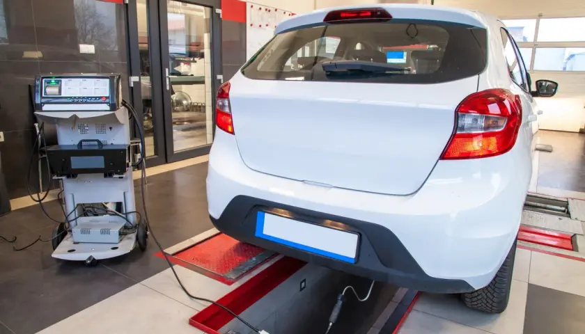 Controllo emissioni per la revisione auto scaduta. Un'auto bianca è collegata a un analizzatore di gas di scarico in un'officina.
