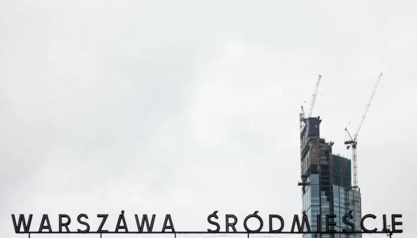 Varso Tower w budowie z dźwigami, na tle napisu "WARSZAWA ŚRÓDMIEŚCIE".