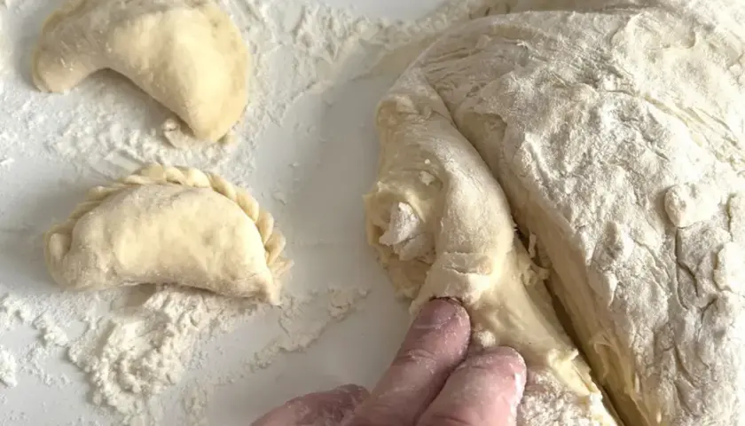 Ręce formują ciasto na pierogi. Wkrótce dowiesz się, ile gotować pierogi, by były idealne.