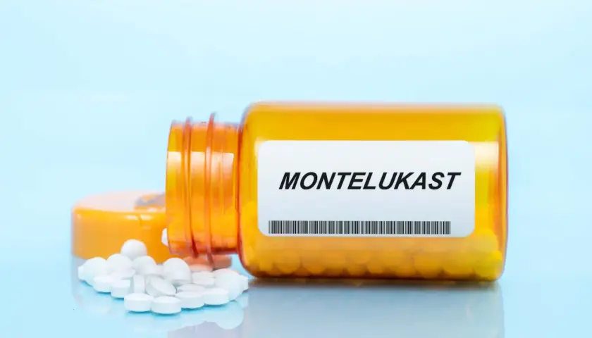Pomarańczowa buteleczka z lekami na astmę, z etykietą "MONTELUKAST" i rozsypanymi tabletkami.