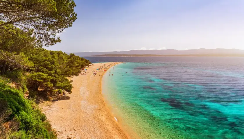 Traumhafter kroatischer Strand mit Pinienwald und türkisfarbenem Wasser. Menschen entspannen sich am Zlatni Rat Strand.