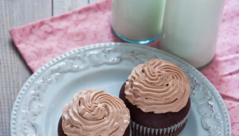 Deux cupcakes au chocolat avec une ganache chocolat passion onctueuse, servis sur une assiette bleue avec deux verres de lait.