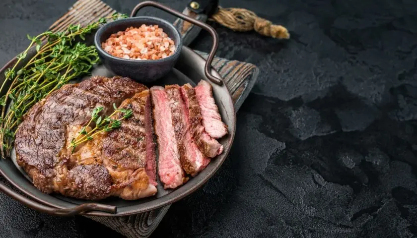 Un succulent entrecôte grillé, tranché et garni de thym frais, servi avec du sel rose sur un plateau.