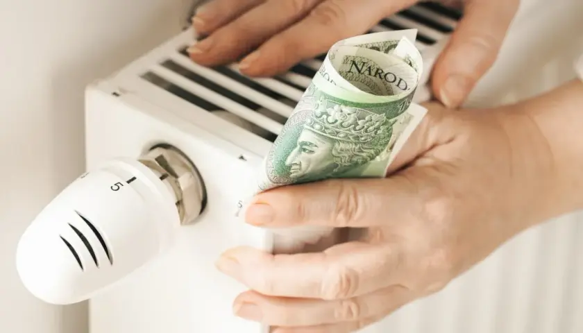 Ręce trzymają banknot 100 zł przy grzejniku. Sprawdzanie rachunków za ogrzewanie, cennik pogotowia gazowego.