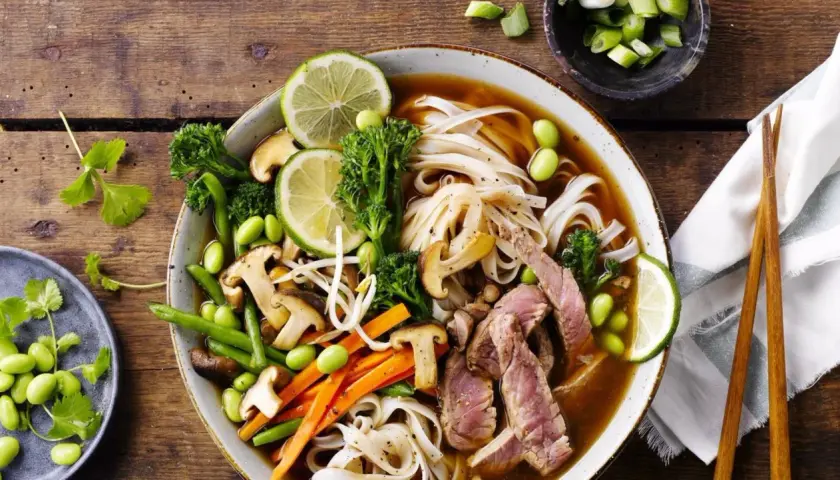 En skål med pho recept med nudlar, biff, grönsaker och lime.
