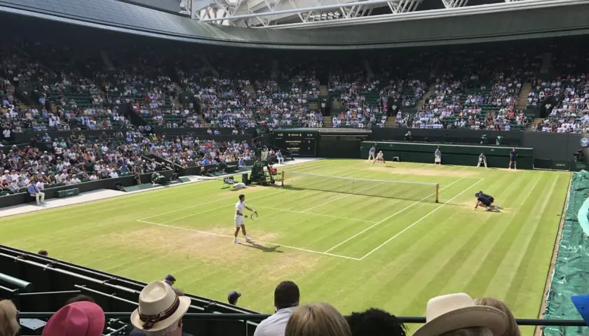 Mecz tenisowy na trawiastym korcie Wimbledonu z widownią na trybunach.